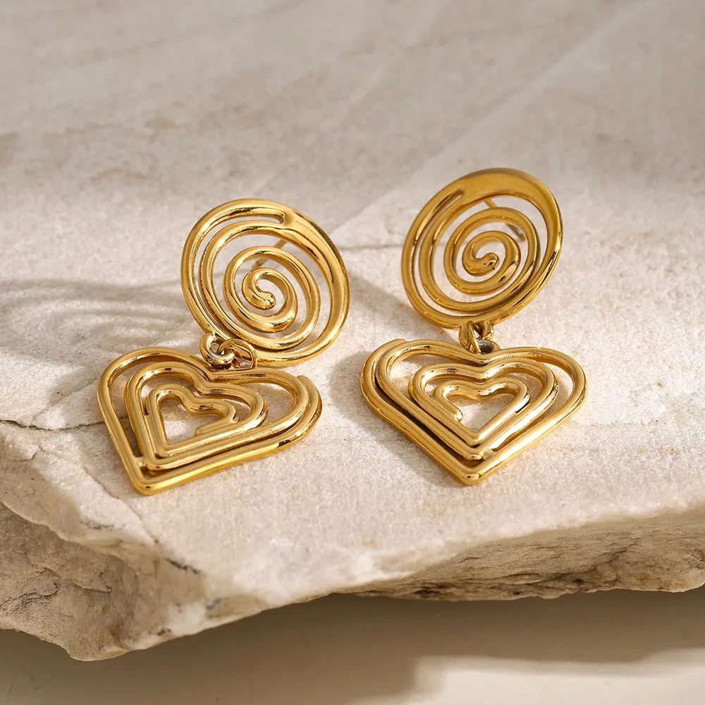 Elegant gold-plated stainless steel heart earrings on a stone surface, showcasing a unique swirl design.