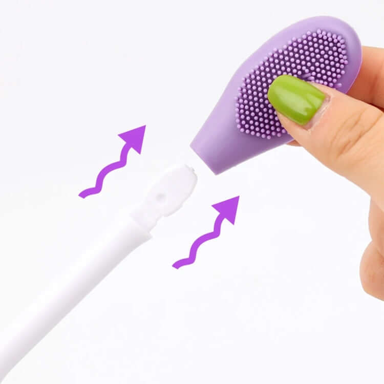 Double-headed silicone face brush with a white handle pressed by a hand on a white background.