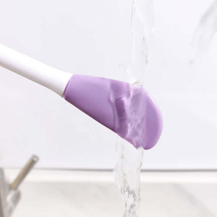 Double-headed silicone face brush head with water flowing from it on a white background.