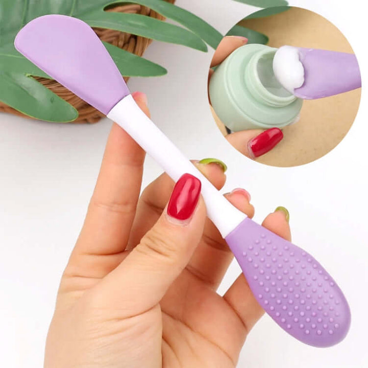 A purple double-headed silicone face brush is held in the hand, and a close-up inset reveals a bottle of cream.