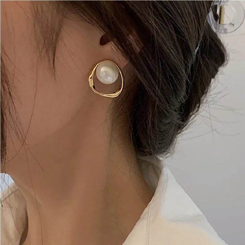 A lady wearing a gold pearl drop earrings against a neutral background