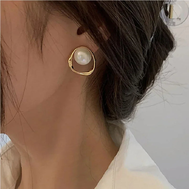 A lady wearing a gold pearl drop earrings against a neutral background