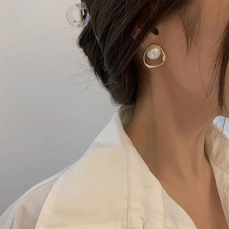 Close-up of a lady wearing a gold pearl drop earring on a neutral background.