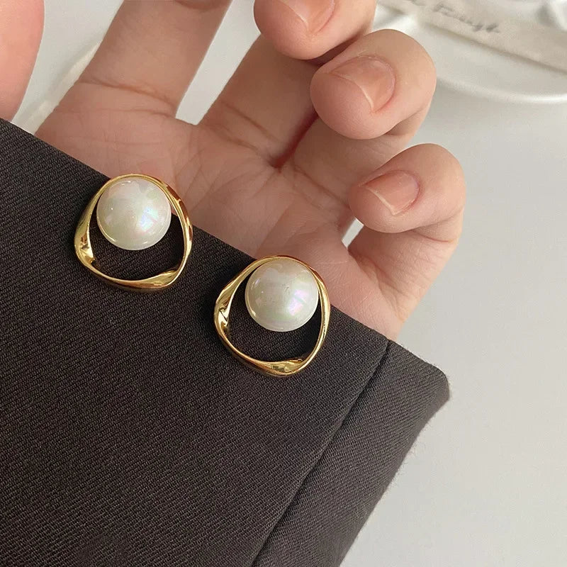 Gold pearl drop earrings held in a hand against a neutral background
