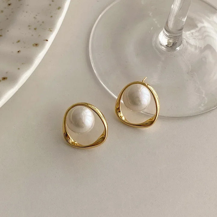 Gold pearl drop earrings on a light surface