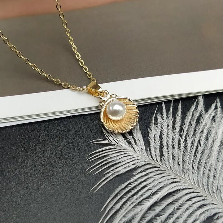 Gold necklace with a shell pendant featuring a pearl on a dark surface with a leaf.