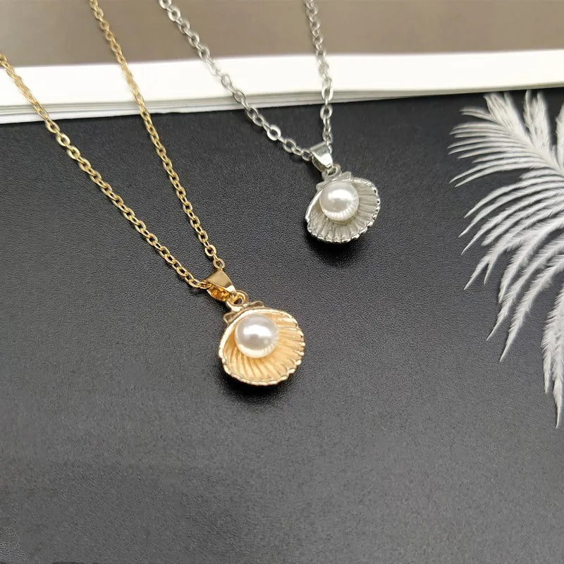 Two necklaces with shell and pearl pendants on a dark surface.