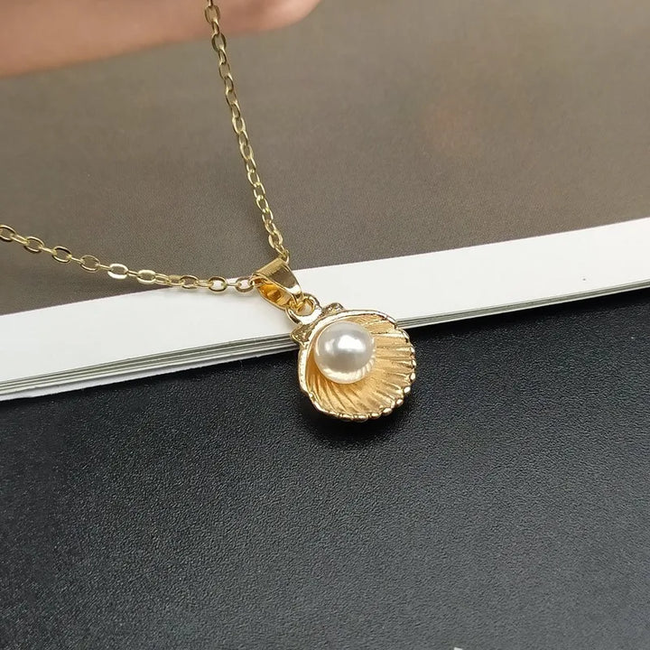 Gold necklace with a shell and pearl pendant on a dark surface