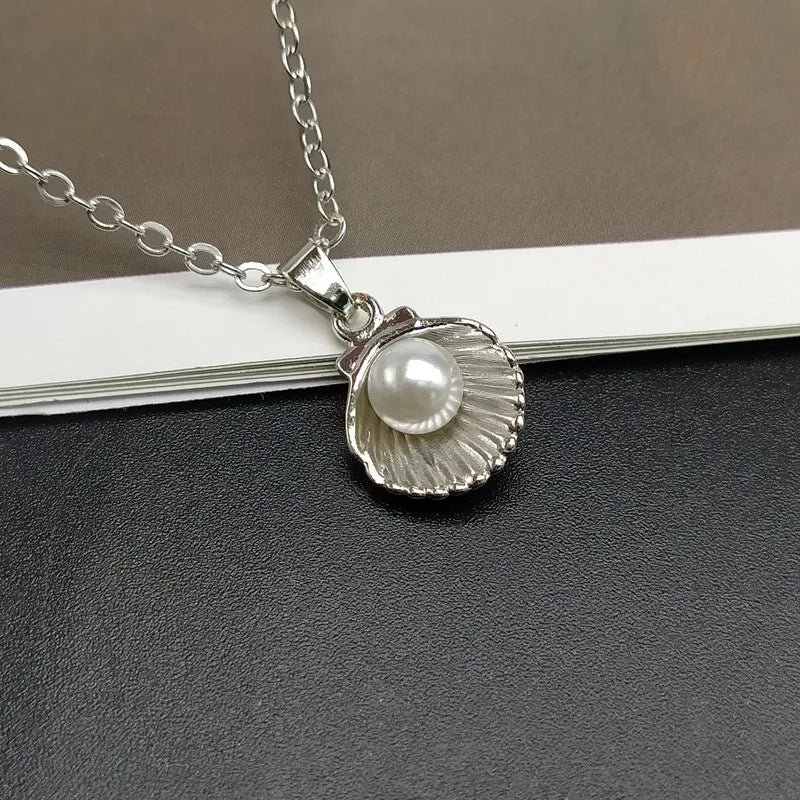 Silver necklace with a shell and pearl pendant on a gray surface