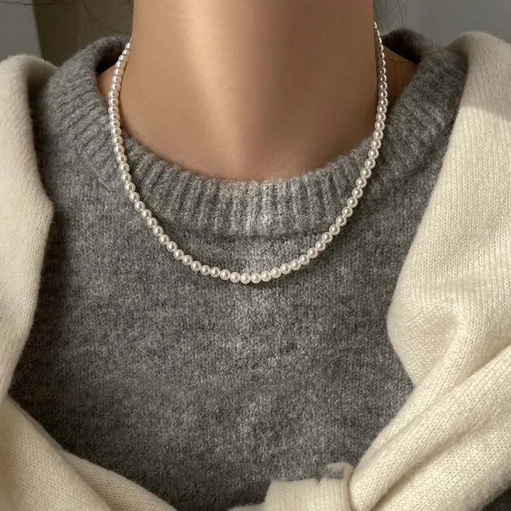 Elegant white pearl necklace worn over a gray sweater, showcasing a stylish magnetic clasp.