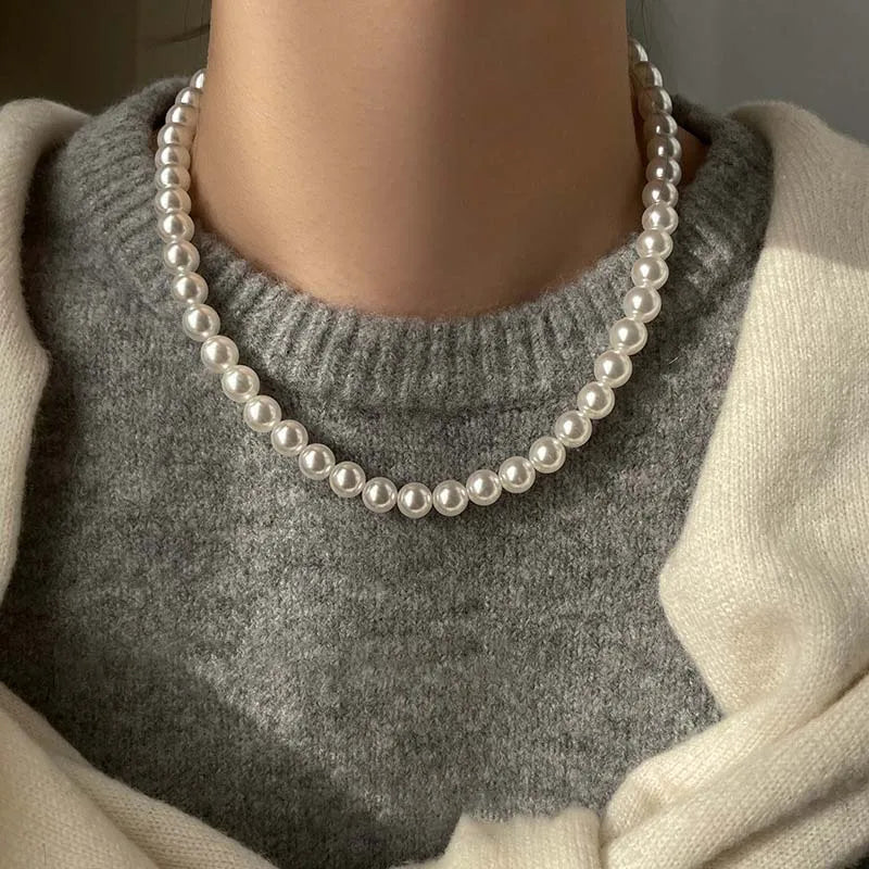 Elegant white pearl necklace worn over a gray sweater, showcasing a classic and sophisticated jewelry style.