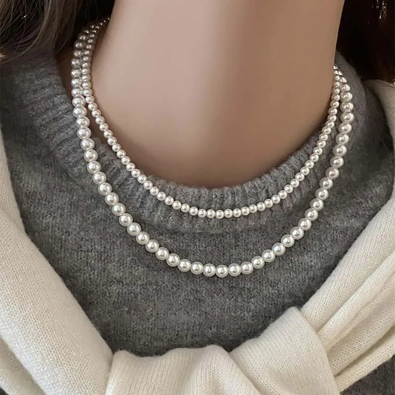 Elegant three-strand white pearl necklace worn over a gray sweater, showcasing its timeless beauty and style.