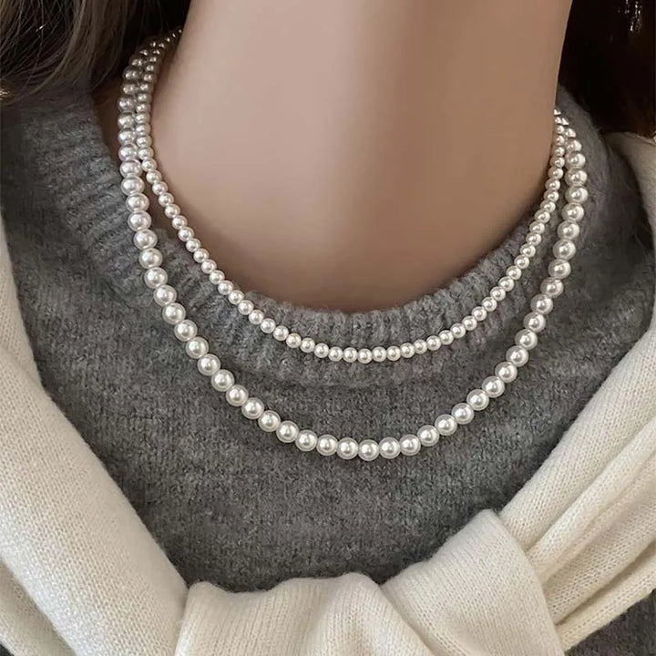 Elegant three-strand white pearl necklace worn over a gray sweater, showcasing its timeless beauty and style.