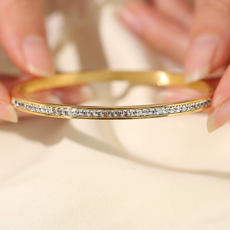 Elegant gold bracelet with sparkling crystals, held delicately by fingers against a soft fabric background.