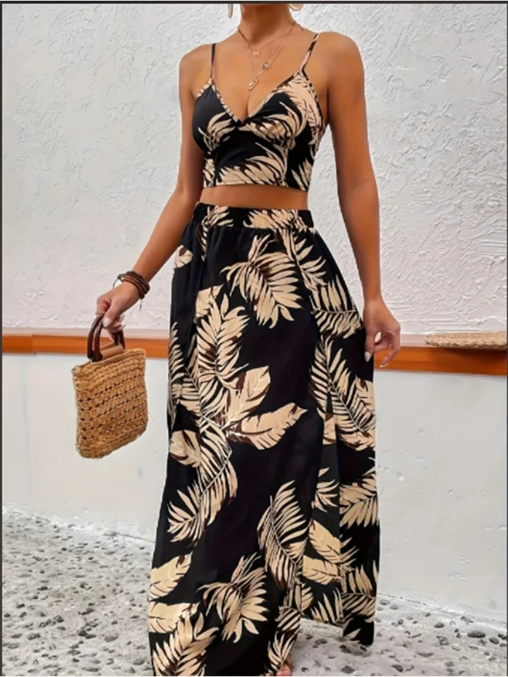 A woman wearing a black summer-printed vest and skirt set holding a woven bag against a white wall.