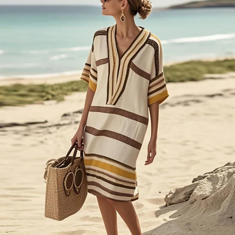 Model in a vintage stripe print midi dress walking on the beach with a straw bag, perfect for summer outings.