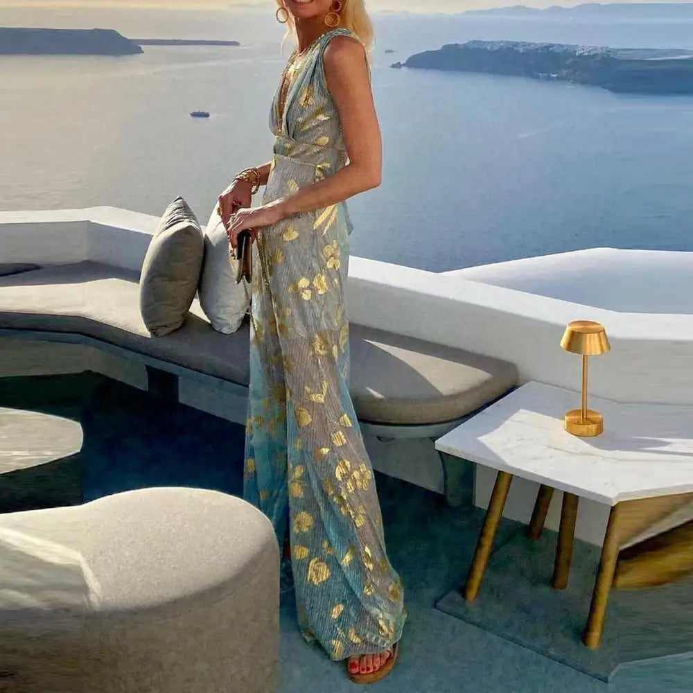 Woman in a long cyan bronzing beach dress standing on a rooftop with a scenic view of the ocean.