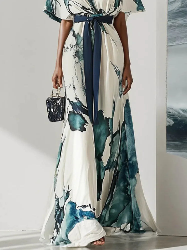 Woman wearing a maxi watercolor dress with a blue belt against a white background